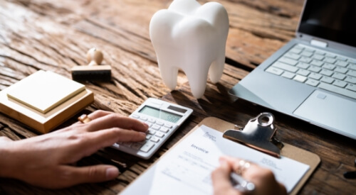 Person at desk typing on calculator and writing on clipboard