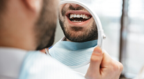 Smiling man looking at his teeth in mirror