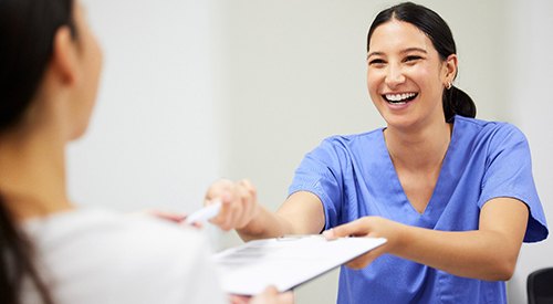 Dental assistant smiling while handing patient form