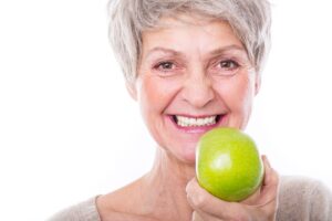 Woman with gray hair smiling holding green apple in front of her face